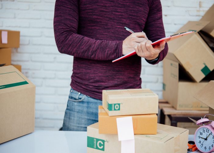 Handsome Young man working with papers among parcels at table in delivery department. online concept